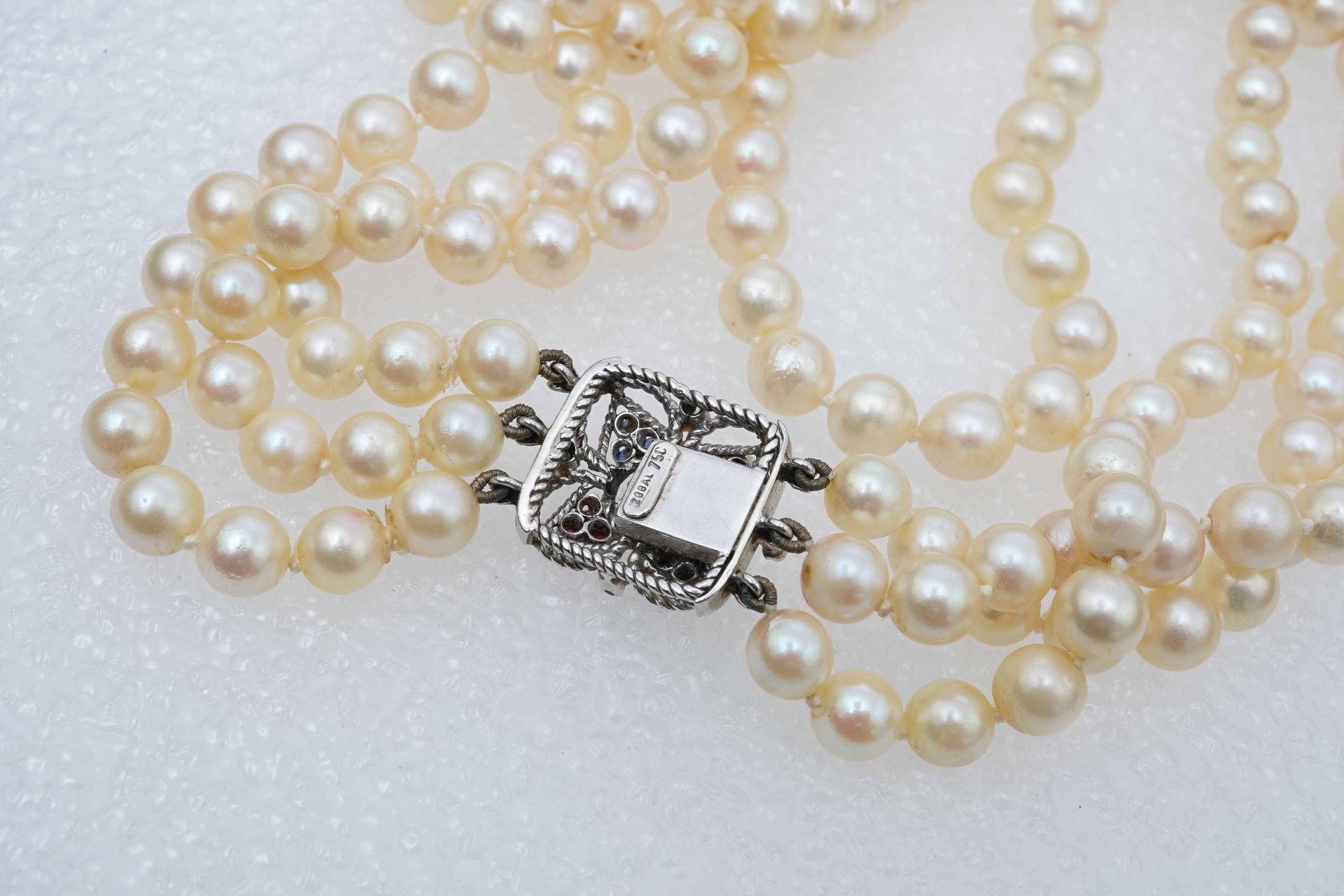 A mid to late 20th century Italian triple strand cultured pearl necklace, with emerald, sapphire and ruby cluster set 750 white metal clasp, 44cm.